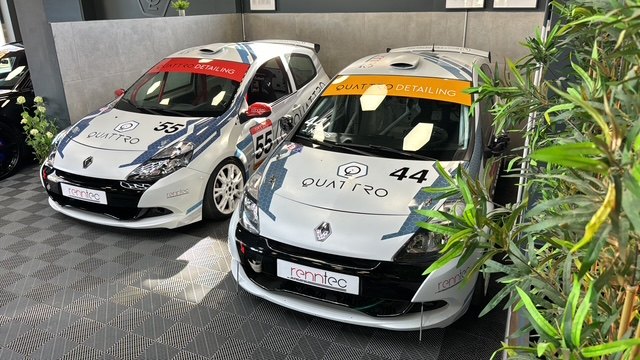 Two Quattro-liveried Renault Clio Cup race cars, numbers 44 and 55, parked in the showroom